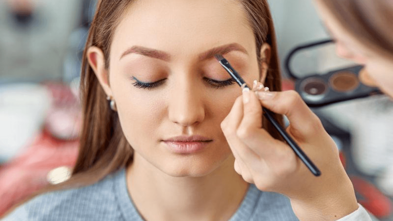 Makeup artist applying eye makeup to a model with blurred background